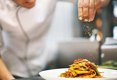 Un chef añadiendo SAZONADOR NATURÍSIMO MAGGI® a un plato.