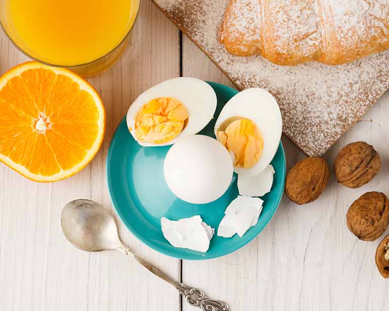 Huevos cocidos, acompañados por jugo de naranja y un croissant.