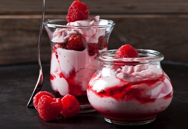 Un postre en vaso con frutos rojos, frutos secos y crema batida.