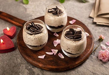 Postre de chocolate y galletas en vaso, sobre una bandeja decorada con pétalos.