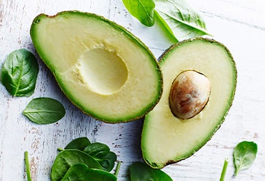 Aguacate partido por la mitad y hojas de espinaca alimentación balanceada