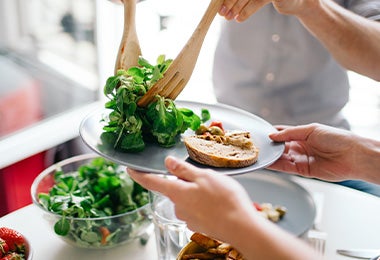 Una persona sirve una comida vegetariana con verduras y pan