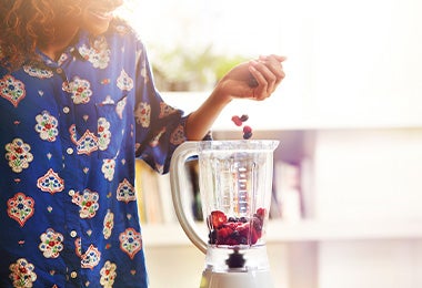 Mujer preparando açaí bowl añadiendo frutas en licuadora