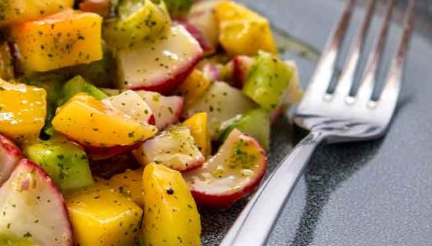 Una ensalada con mango y verduras, con su aderezo.