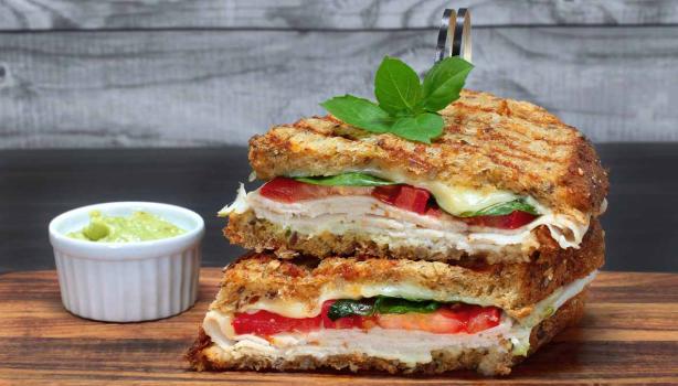 Pan panini relleno de jamón, tomate y albahaca, acompañado con salsa