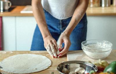 Mujer con utensilios e ingredientes preparando masa para pizza