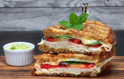 Pan panini relleno de jamón, tomate y albahaca, acompañado con salsa