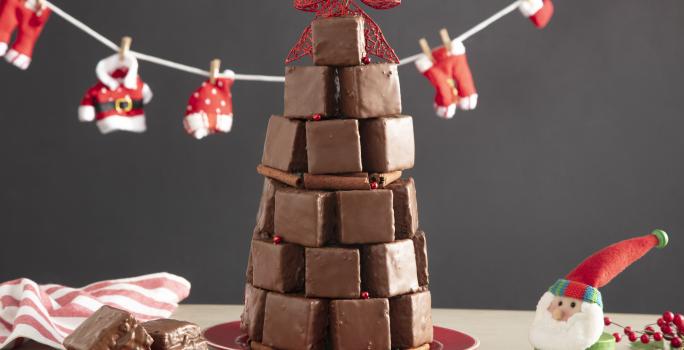 Fotografía en tonos rojos sobre un banco de madera con un pequeño tendedero de Papá Noel, un adorno de Papá Noel en el lado derecho, un plato pequeño con dos bollos y en el centro varios bollos formando un árbol de Navidad.